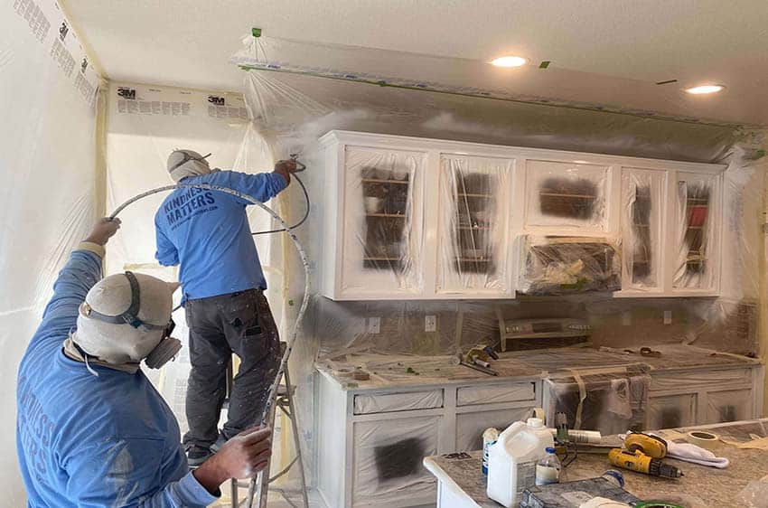 Two paint crew members spraying interior cabinets white