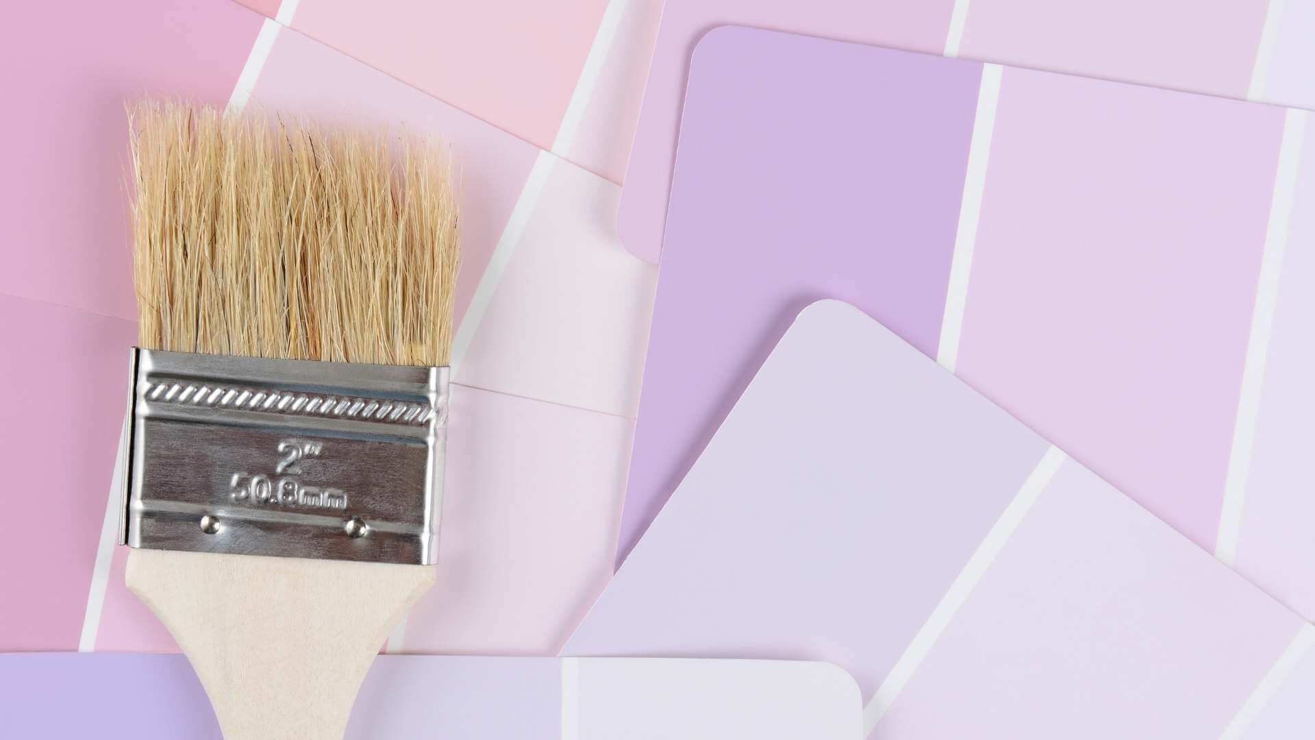 A paint brush laying on top of pink and purple paint color swatches